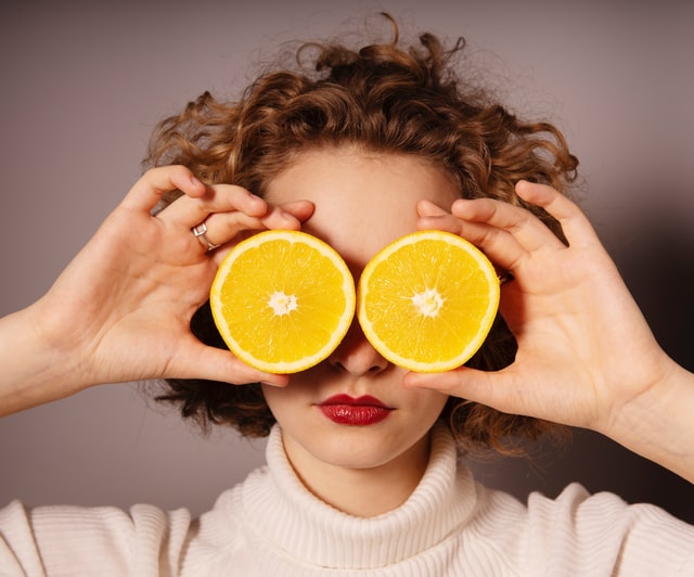 Woman relaxing with oranges on her eyes, representing self-care and healthy skin