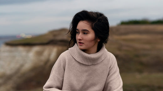 Woman wearing a chunky white sweater on the beach, representing winter immunity and wellness.