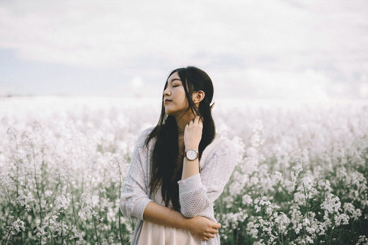 Asian woman surrounded by white flowers, showcasing multitasking skincare products